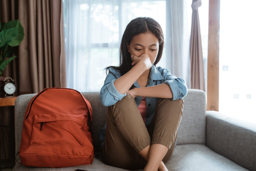 a teen sitting on the couch covers her face and looks worried about her suicidal friend