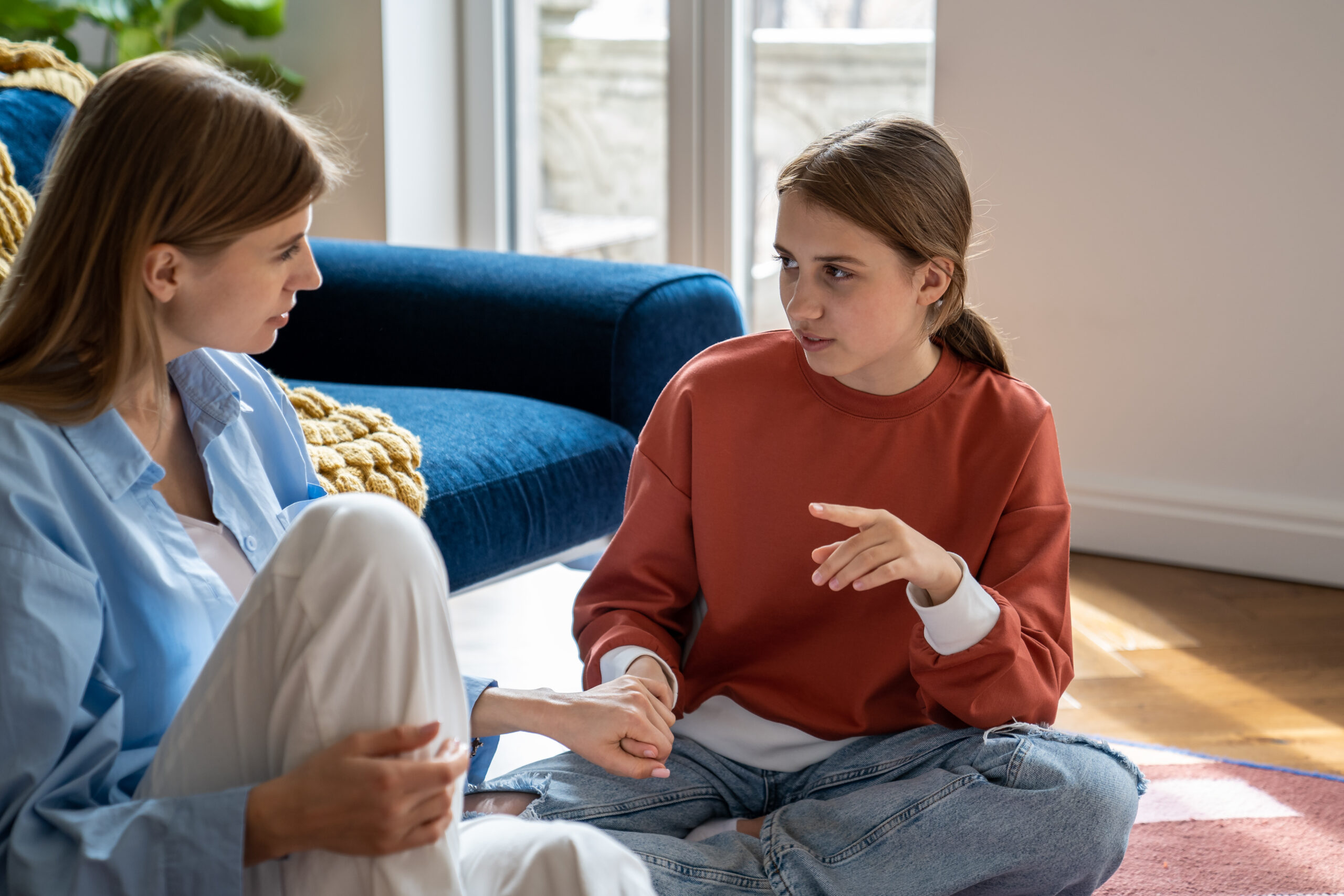 A parent and teenager sitting comfortably at home, engaged in a calm, open, and supportive conversation.