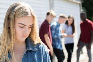 An upset teen stands alone away from a group of other teens