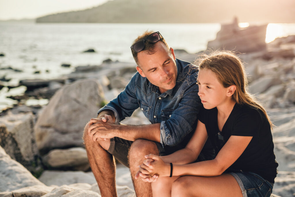 a dad talks to his teen about how to manage stress and anxiety as they sit outside by the water