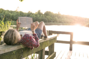 teen girl reading on a dock by a lake
