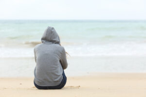 back of teen girl sitting on beach at ocean